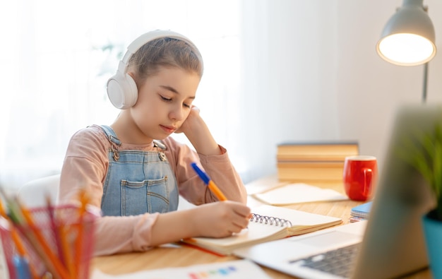 Retour à l'école. Un enfant heureux est assis au bureau. Fille faisant ses devoirs ou éducation en ligne.