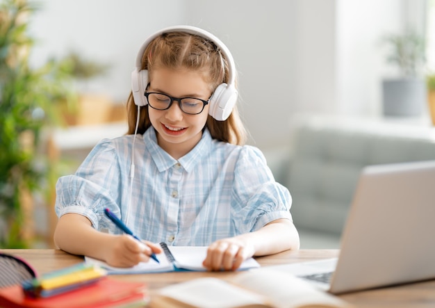 Retour à l'école. Un enfant heureux est assis au bureau. Fille faisant ses devoirs ou éducation en ligne.