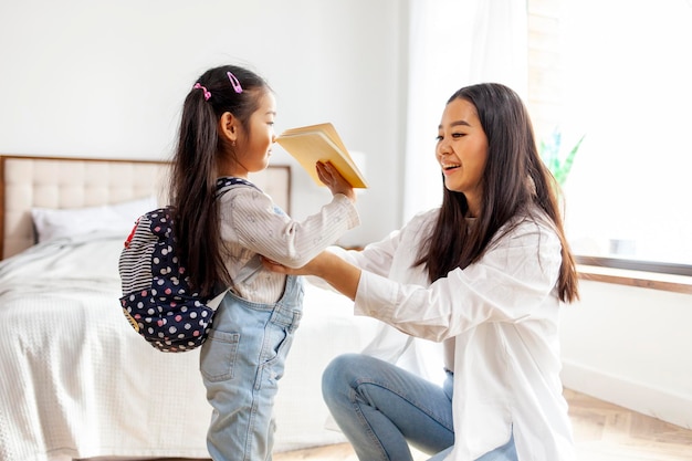 retour à l'école fille asiatique tenant un cahier à la maison le matin une femme coréenne aide sa fille