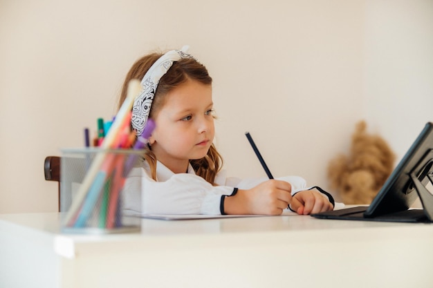 Retour à l'école Heureuse petite écolière assise à son bureau La fille fait ses devoirs à l'aide d'un ordinateur tablette éducation en ligne