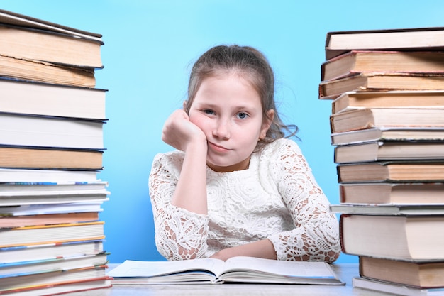 Retour à l'école. Heureux enfant industrieux mignon est assis à un bureau à l'intérieur. L'enfant apprend en classe en apprenant à la maison.Montagnes de livres sur les côtés