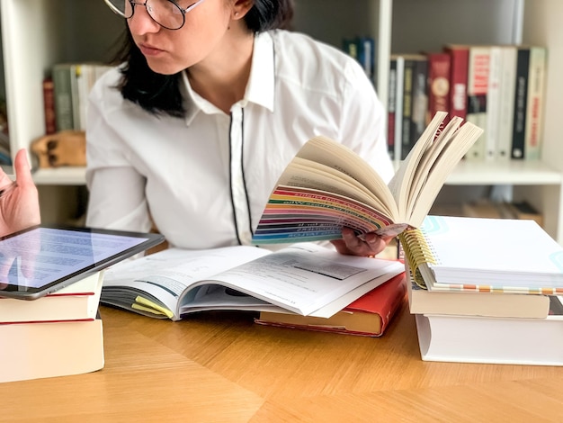 De retour à l'école, une jeune étudiante du millénaire étudie à la maison avec une pile de livres et une tablette.