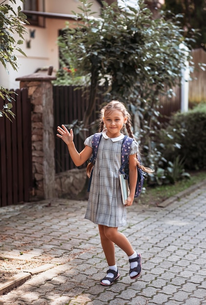 Retour à l'école Une jolie petite écolière vêtue d'une robe à nattes et d'un grand sac à dos bleu tient des livres et se promène dans la cour de l'école Une petite fille va en première année