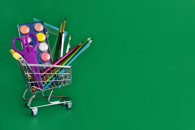 Retour à l'école. Mini caddie avec crayons et fournitures scolaires sur fond vert. Bannière de l'école