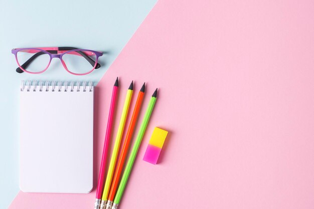 Photo retour à l'école mise en page pour la publicité des fournitures scolaires fond bleu et rose avec des cahiers blancs crayons au néon brillants gomme à effacer focalisation sélective