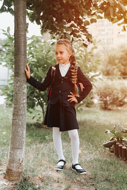 Retour à l'école petit enfant heureux élève écolière de huit ans en uniforme de mode avec sac à dos et coiffure volumineuse longue tresse prête à aller en deuxième année premier jour à l'école primaire flare