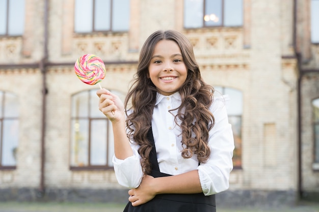 Retour à l'école. petite fille souriante avec des dents saines. écolière heureuse en uniforme élégant. bonheur d'enfance. mode enfant et coiffeur. petite étudiante tient des bonbons à la sucette.