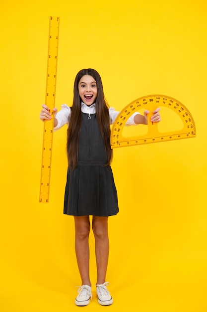 Photo retour à l'école school girl tenir la règle de mesure isolé sur fond jaune visage excité émotions joyeuses de l'adolescente