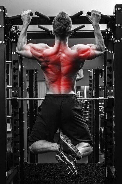 Retour spécialisation en bodybuilidng. Homme musclé faisant des tractions sur une barre horizontale.