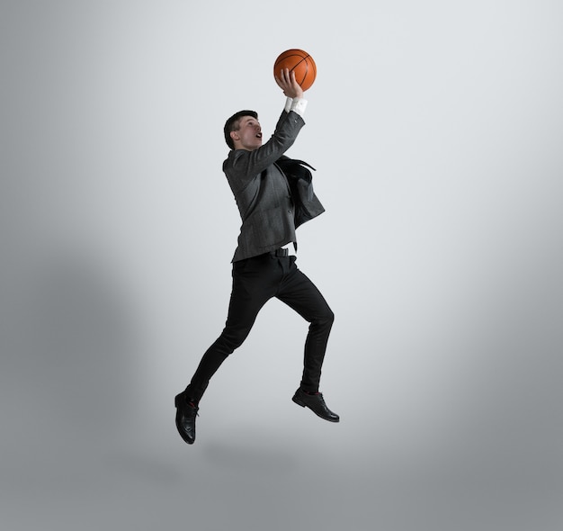 Photo de retour à l'université, il n'est jamais trop tard pour devenir une star du sport. l'homme en vêtements de bureau s'entraîne au basket-ball sur un mur gris. look inhabituel pour homme d'affaires en mouvement, action. sport, mode de vie sain.
