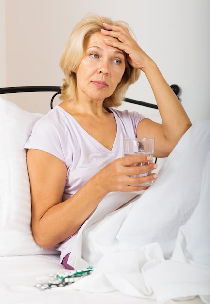 retraité au lit avec des pilules et un verre d&#39;eau