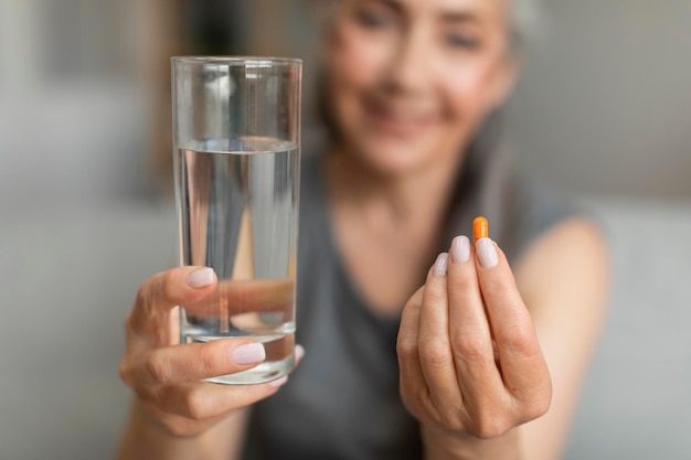 Une retraitée caucasienne souriante montre un verre d'eau et une pilule de vitamines analgésiques ou