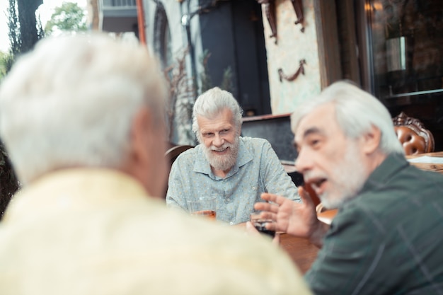 Des retraités qui parlent. Hommes aux cheveux gris à la retraite parlant et buvant de l'alcool à l'extérieur