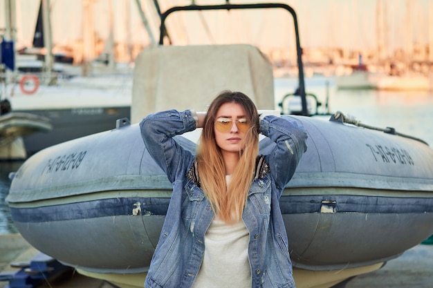 Rétro-éclairage doré, belle fille à lunettes de soleil et une veste en jean avec de longs cheveux blonds au coucher du soleil d'été