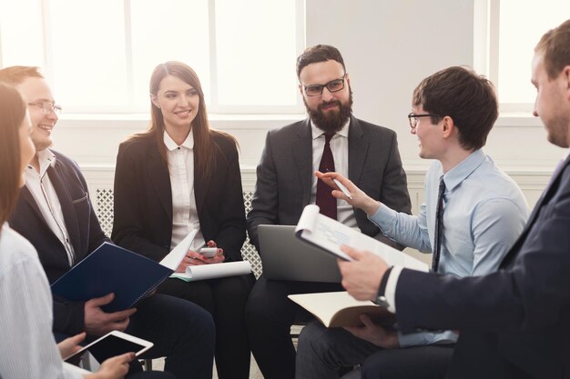 Réunion d'affaires. Jeunes hommes et femmes d'affaires heureux au bureau moderne, discussion amicale d'équipe sur le lieu de travail. Brainstorming et communication avec les partenaires pour le démarrage, planification de la stratégie de développement