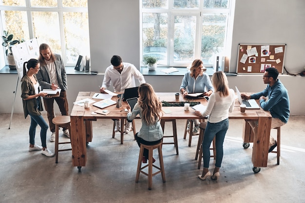 Réunion de jour. Vue de dessus des jeunes modernes communiquant tout en travaillant ensemble dans la salle du conseil