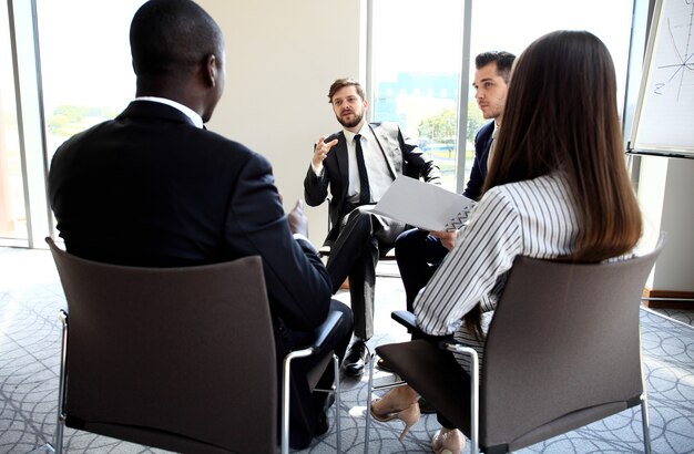 Photo réunion en matinée. groupe de cinq jeunes discutant de quelque chose assis à la table au bureau ensemble