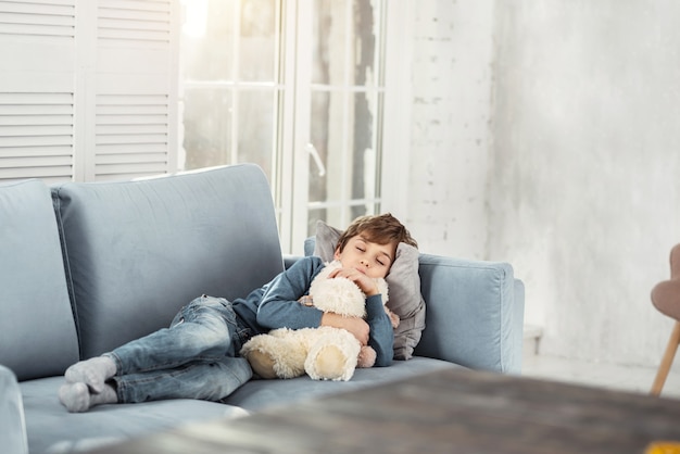 Rêve. Mignon Petit Garçon Blond étreignant Son Joli Jouet Préféré Et Allongé Sur Le Canapé Confortable Tout En Faisant Une Sieste