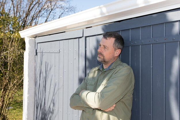 Rêve en plein air bel homme d'âge moyen pensant dans la porte de garage de la maison dans le jardin de la maison