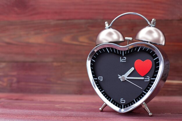 Photo réveil en acier sous la forme d'un coeur avec un coeur rouge sur un fond de bois rose saint valentin