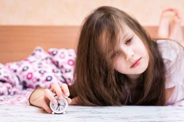 Réveil blanc se dresse sur la table sur le fond d'une fille qui se réveille