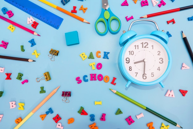 Photo réveil crayons de couleur et fournitures scolaires diverses sur fond bleu. notion d'école. retour à l'école.