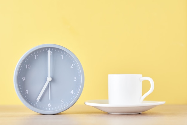 Réveil gris classique et tasse à café blanche sur fond jaune