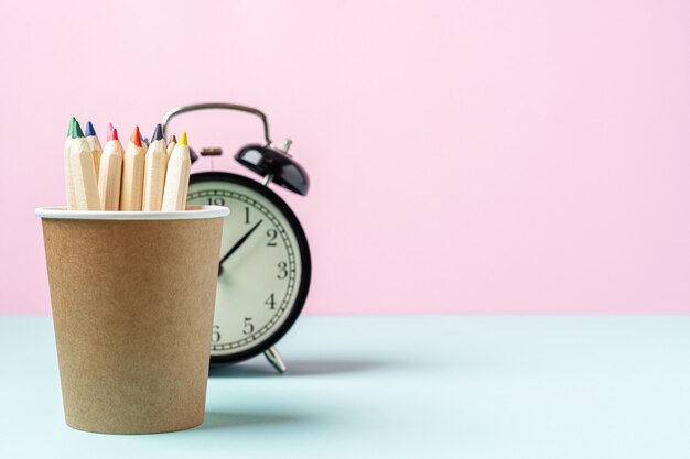 Réveil noir et crayon dans une tasse de café sur rose et bleu