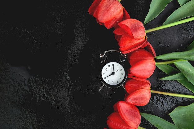 Réveil noir près de bouquet de tulipes rouges. Fête des mères ou des femmes. Carte de voeux. Bonjour le petit déjeuner. Copiez l'espace. Printemps.