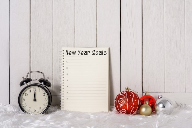 Réveil avec des ornements de Noël et la liste des objectifs du nouvel an écrite sur ordinateur portable avec fourrure blanche