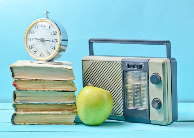 Réveil sur pile de vieux livres, récepteur radio, pomme sur un bleu.