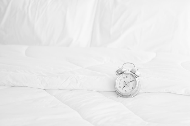 Un réveil placé sur un matelas blanc à la lumière du matin avec espace de copie