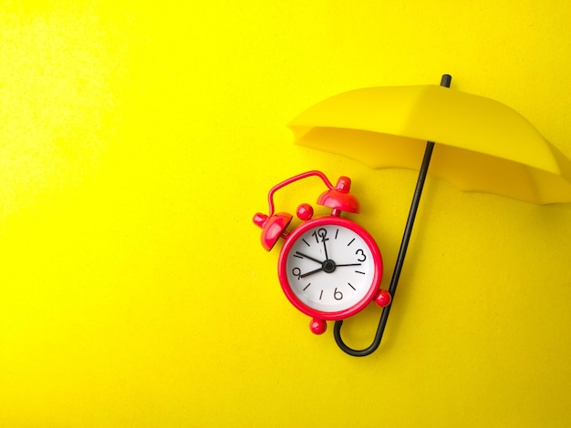 Un réveil rouge avec parapluie jaune sur fond jaune avec espace de copie