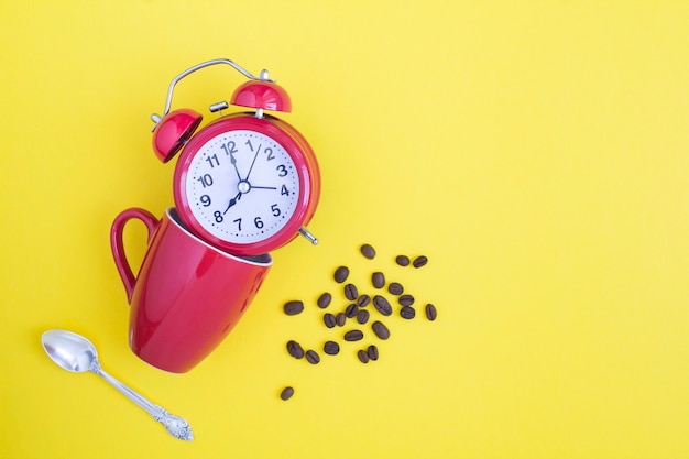 Réveil rouge, tasse rouge et grains de café sur jaune