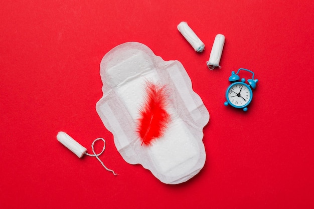 Réveil sonnant avec des tampons hygiéniques féminins et des serviettes hygiéniques menstruelles Concept médical des jours critiques de la femme et de la menstruation Hygiène quotidienne féminine Espace de copie