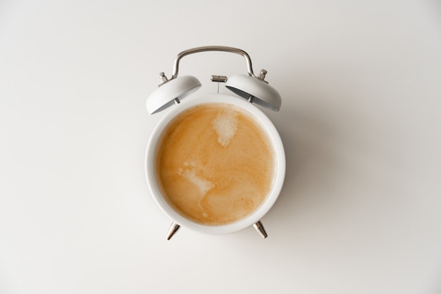 Réveil avec une tasse de café sur fond blanc. concept d'ascensions tôt le matin. premier quart de travail à l'école ou au travail. petit-déjeuner