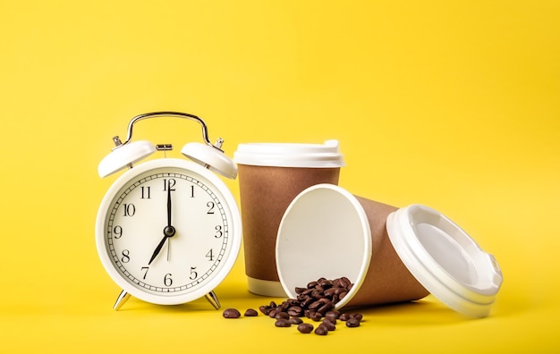 Réveil tasse en papier et grains de café sur fond jaune isolé