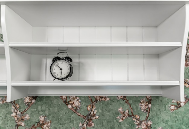 Réveil vintage classique sur une étagère blanche vide dans un intérieur de chambre.