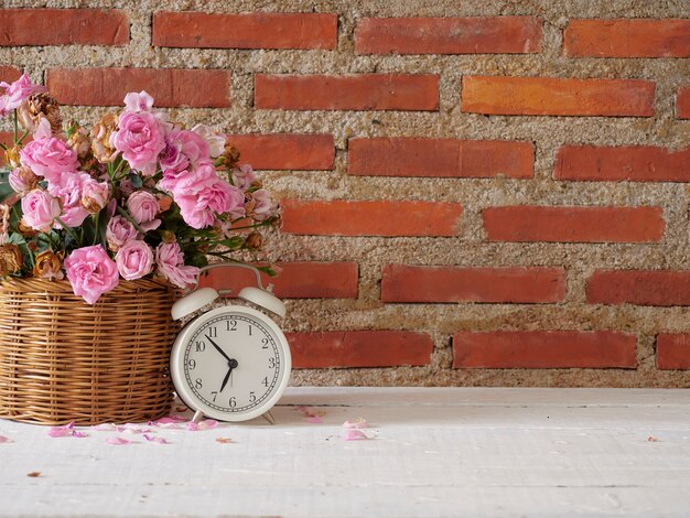 Réveil vintage avec des roses dans le panier sur une table en bois blanc