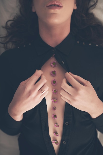 Révélant sa beauté intérieure Prise de vue en grand angle d'une jeune femme non identifiable ouvrant sa chemise au lit pour révéler des fleurs sur sa poitrine