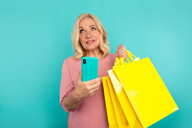 Rêver de belle femme tenant des sacs et un téléphone isolé dans le studio bleu.