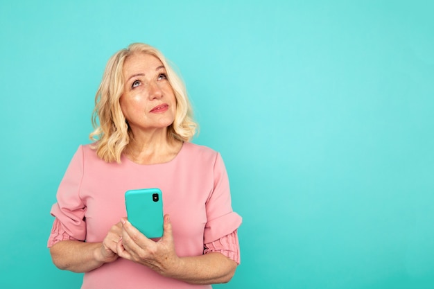 Rêver de femme tenant un téléphone isolé sur le studio bleu.