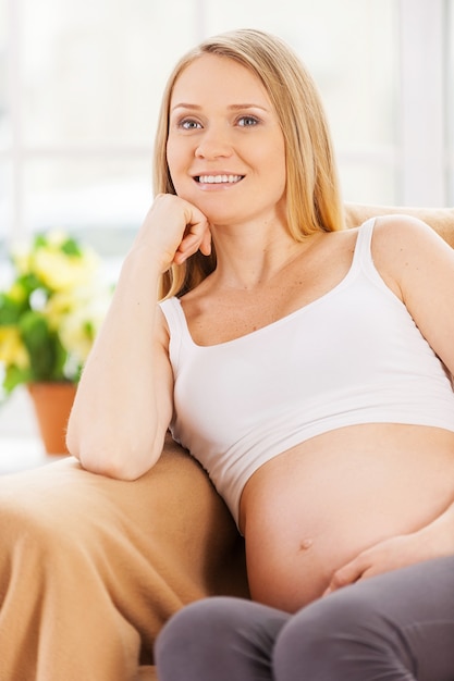 Rêver de jour de femme enceinte. Heureuse femme enceinte assise sur la chaise et tenant la main sur le menton