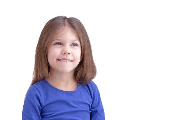 Rêver de sourire heureux lèvre mordante enfant enfant isolé sur fond blanc regardant de côté la taille jusqu'à la petite fille caucasienne de 5 ans en bleu