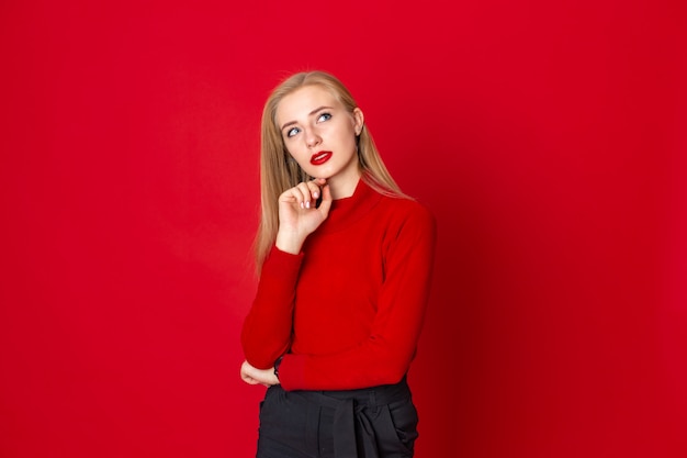 Rêveuse belle femme blonde debout sur un fond rouge