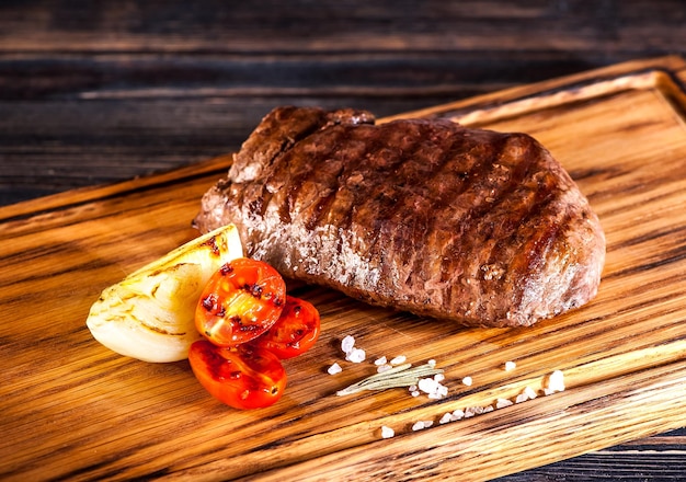 Ribeye de bifteck grillé moyen rare avec des oignons frits et des tomates cerises sur une planche de bois