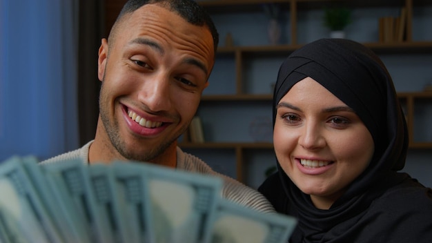 Riche couple multiracial afro-américain comptant des dollars d'argent avec une femme musulmane arabe en hijab