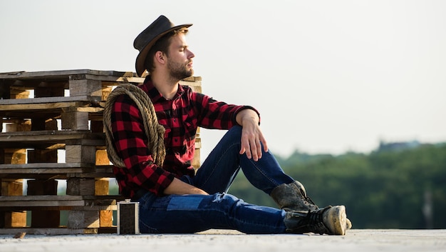 Ride away western cowboy portrait wild west rodeo Homme pensif au chapeau boire du whisky cowboy avec corde de lasso Homme occidental chemise à carreaux sur le ranch Homme de style vintage Cowboy rétro du Far West