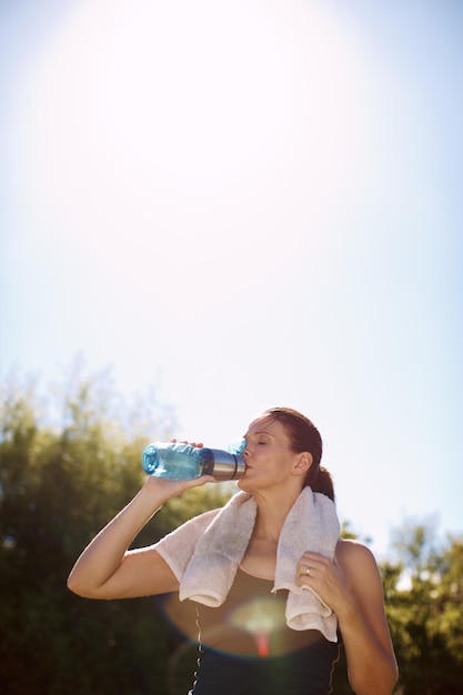 Rien n'est plus rafraîchissant par une chaude journée Une jolie femme buvant de sa bouteille d'eau après une séance d'entraînement