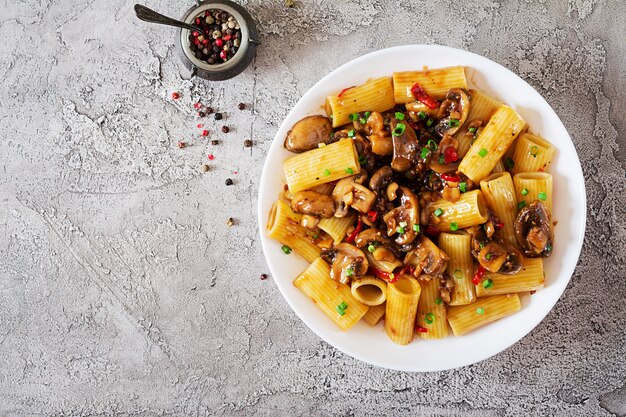 Rigatoni de pâtes végétariennes aux champignons et piments dans un bol blanc sur une table grise. Nourriture végétalienne. Mise à plat. Vue de dessus